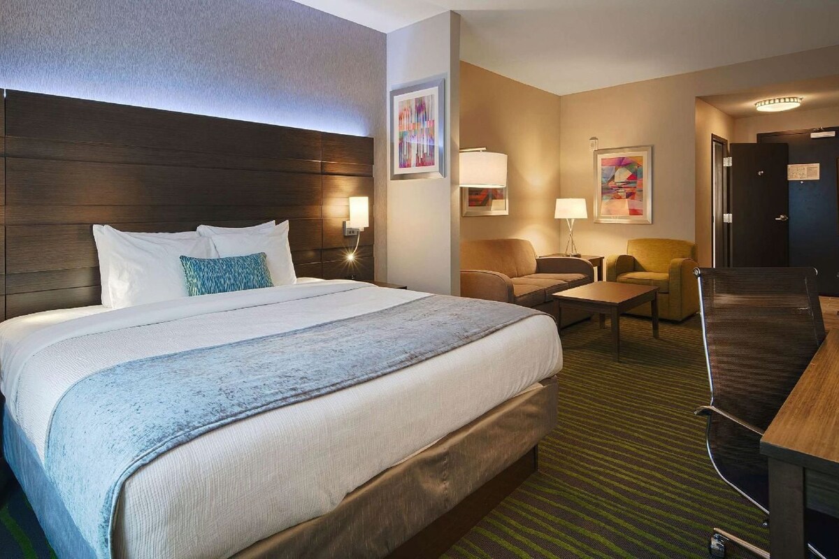 A hotel room with a large bed, a desk, a chair, and a television.