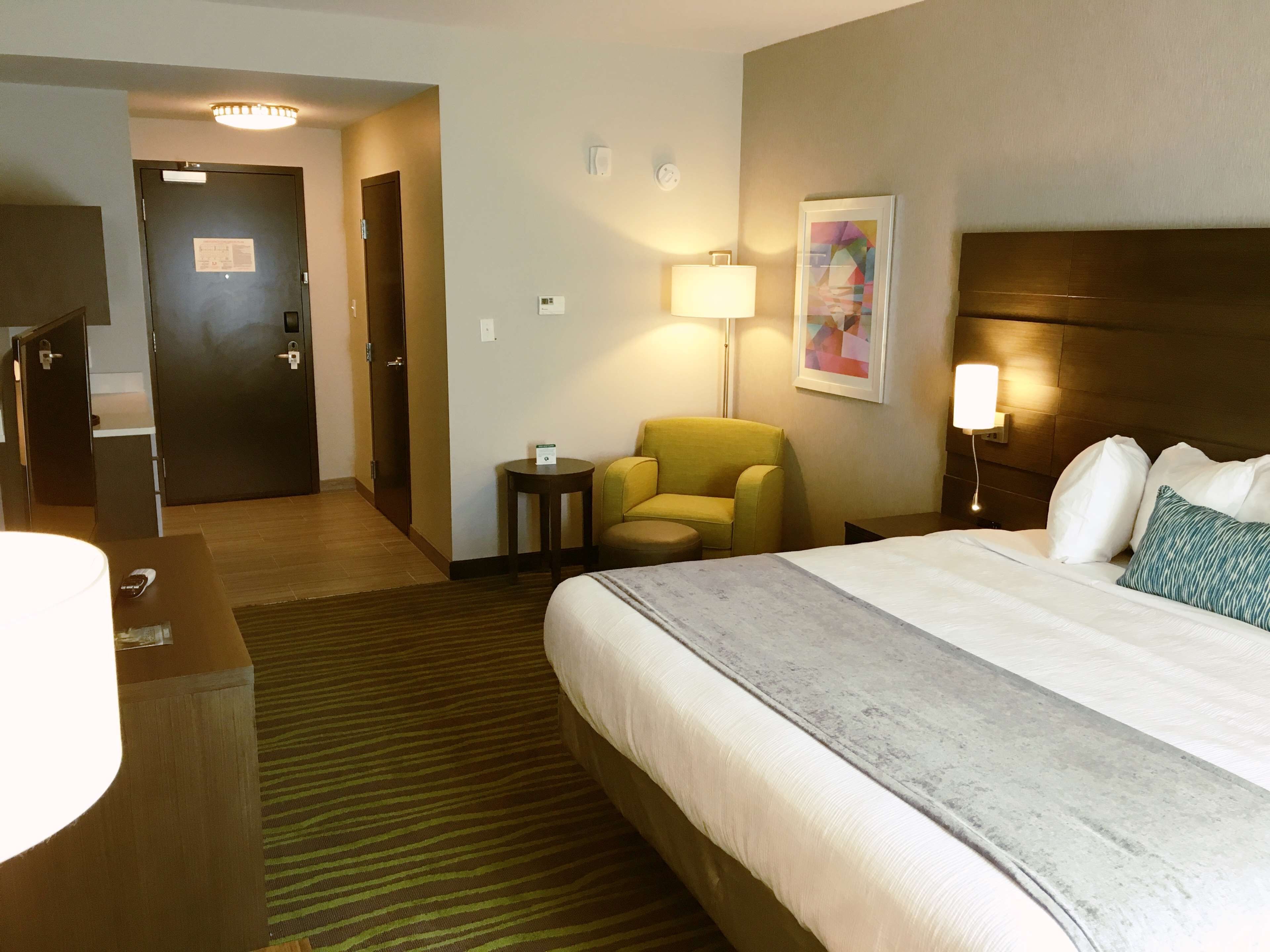 A hotel room with a bed, a desk, a chair, a lamp, and a painting on the wall.