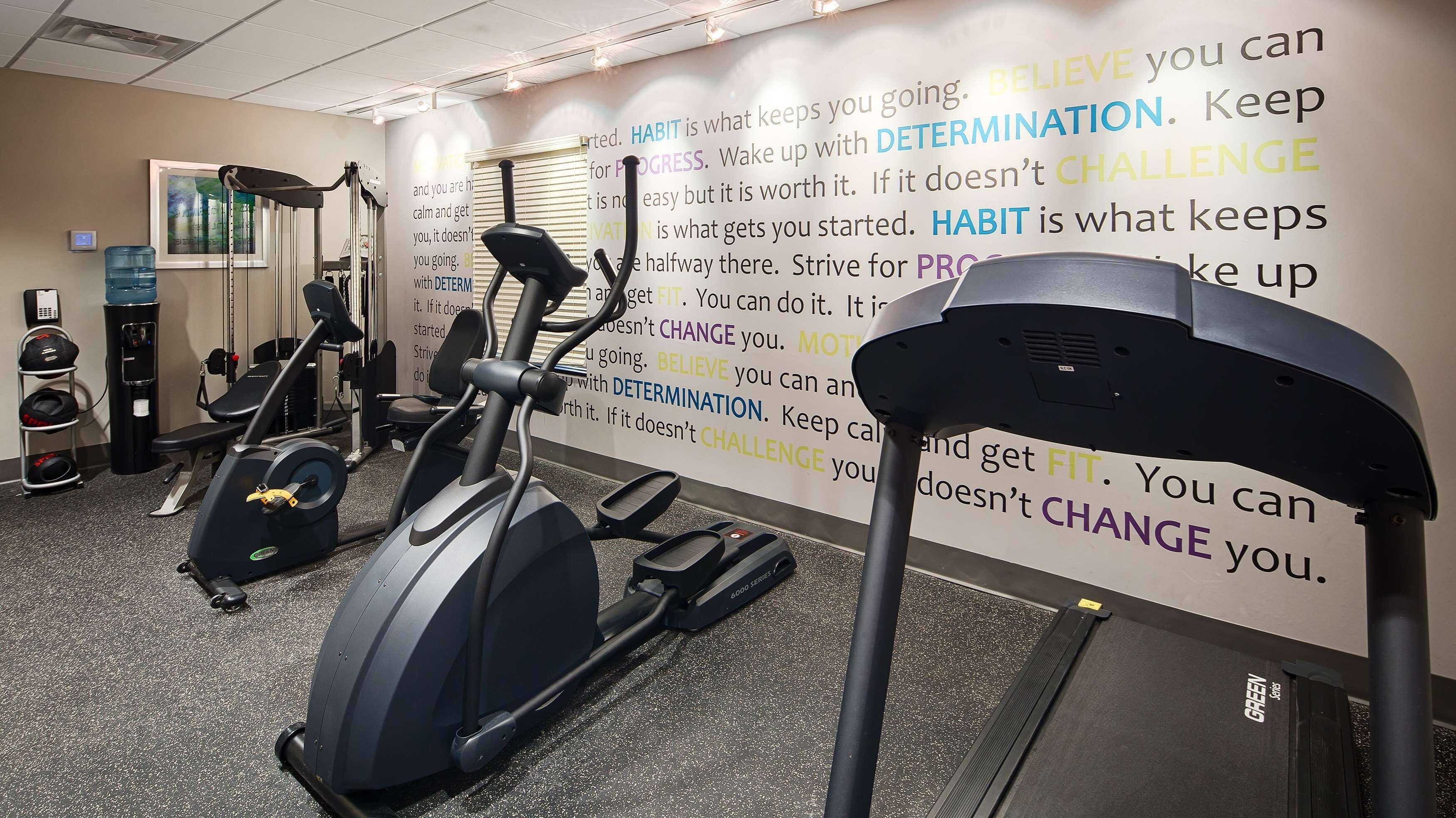 A gym with treadmills, a water dispenser, and motivational posters on the wall.