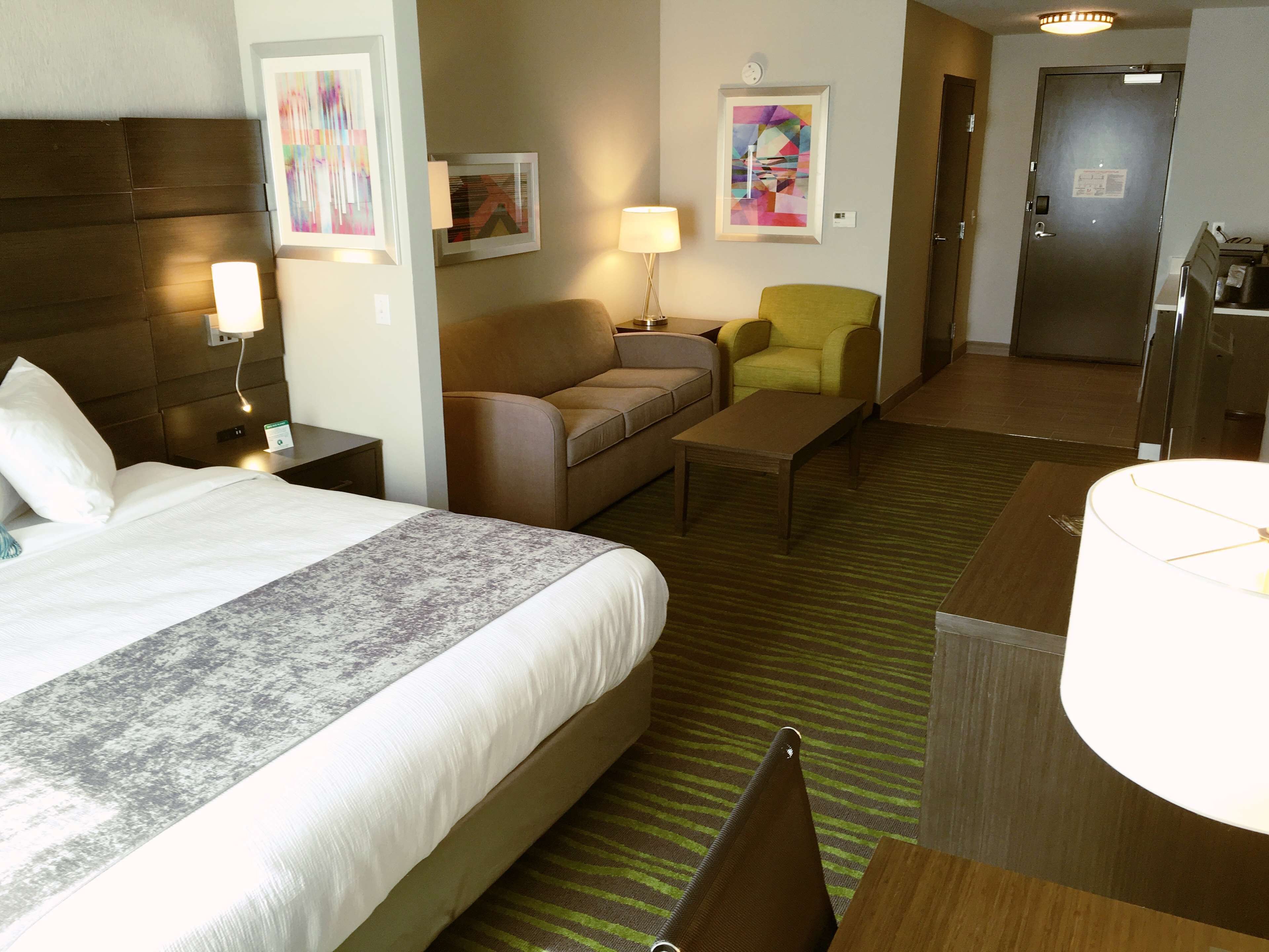 Ein Hotelzimmer mit Bett, Sofa, Sessel, Couchtisch und Schreibtisch mit Lampe.