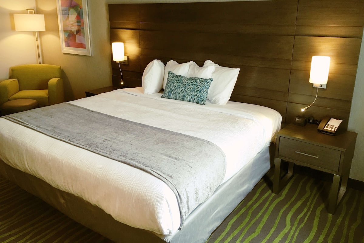 A hotel room with a large bed, two bedside lamps, a chair, a bedside table with a phone, and a painting on the wall.