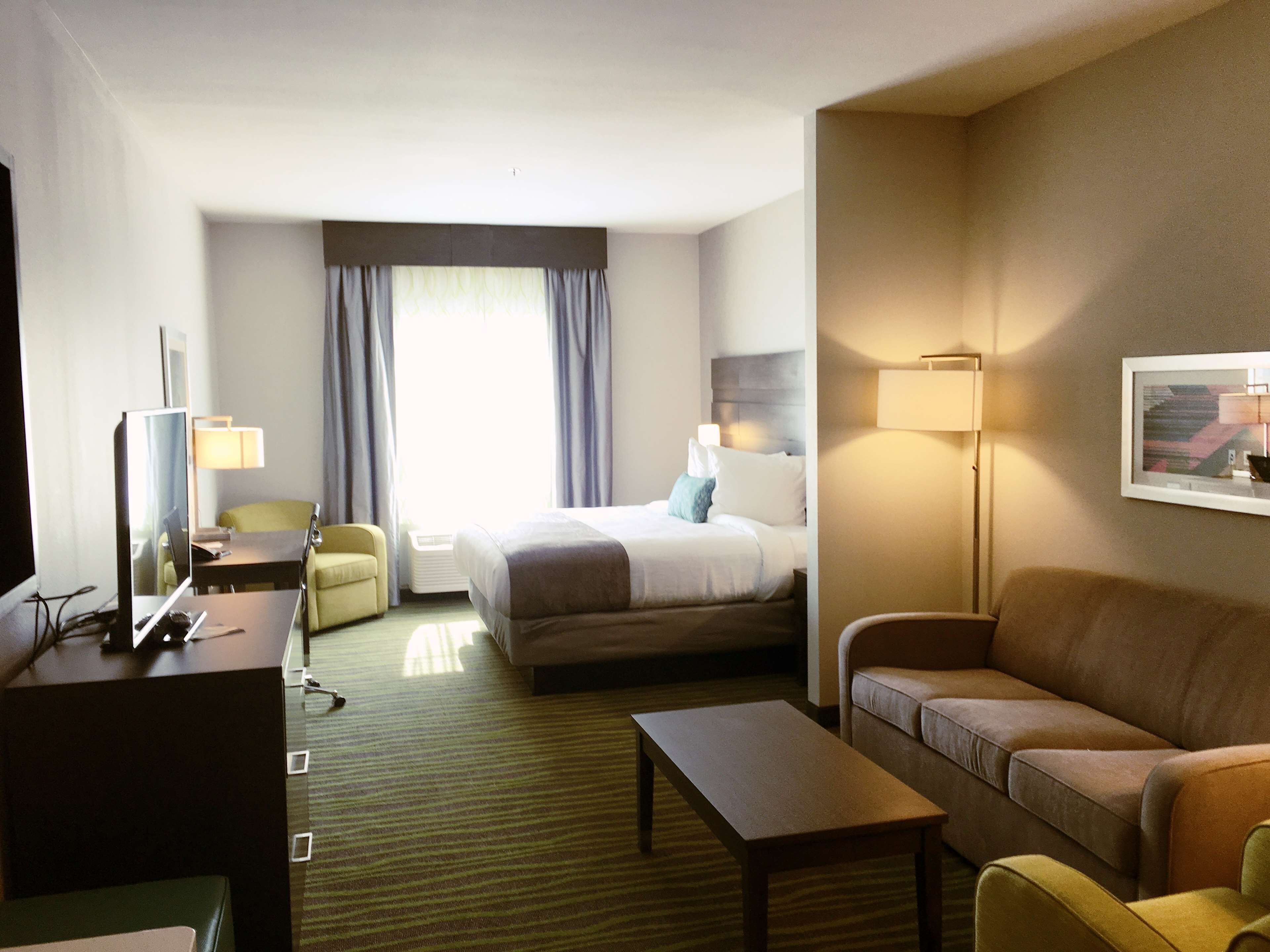 A hotel room with a bed, a desk with a computer, a sofa, a coffee table, and a TV.