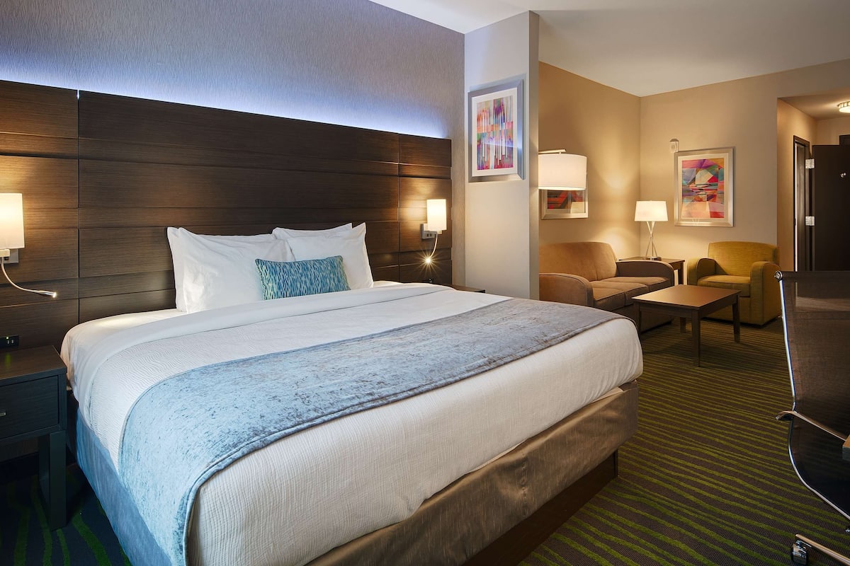 A hotel room with a large bed, bedside tables, a desk, a chair, and artwork on the walls.