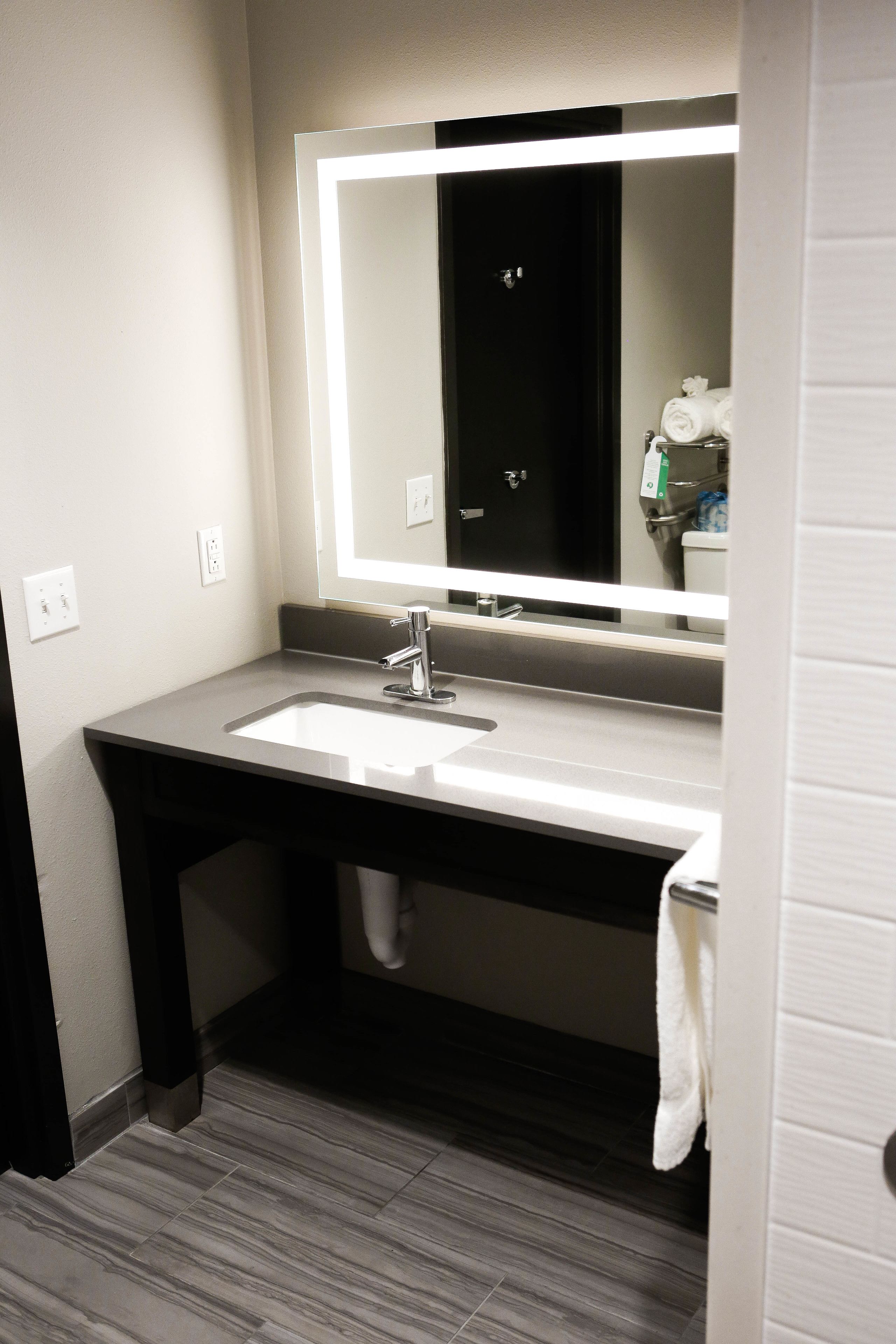 A bathroom with a white sink, a mirror with a lighted frame, a dark wooden vanity, and a towel hanging on the wall.