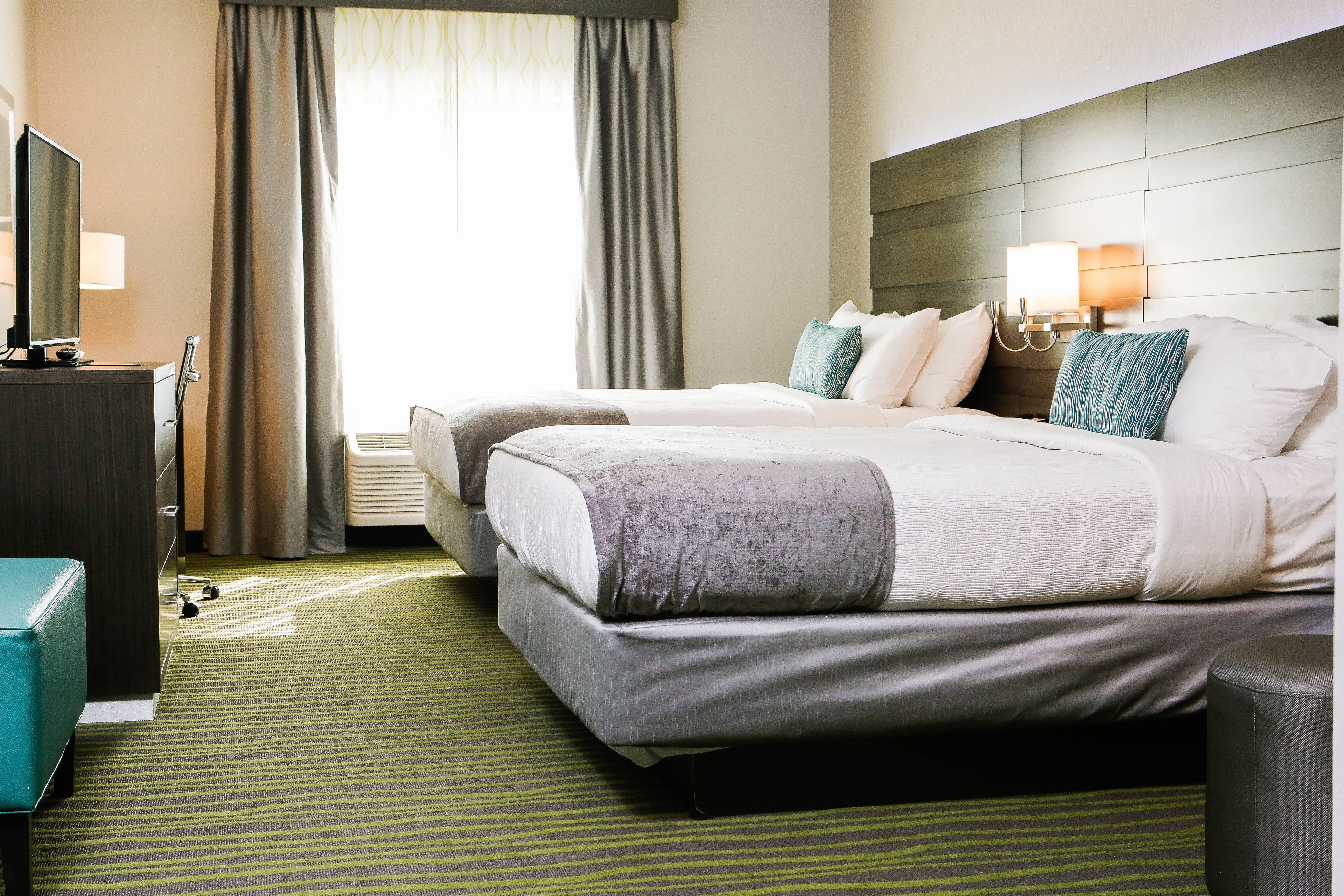 A hotel room with two beds, a television, a desk, and a window with curtains.
