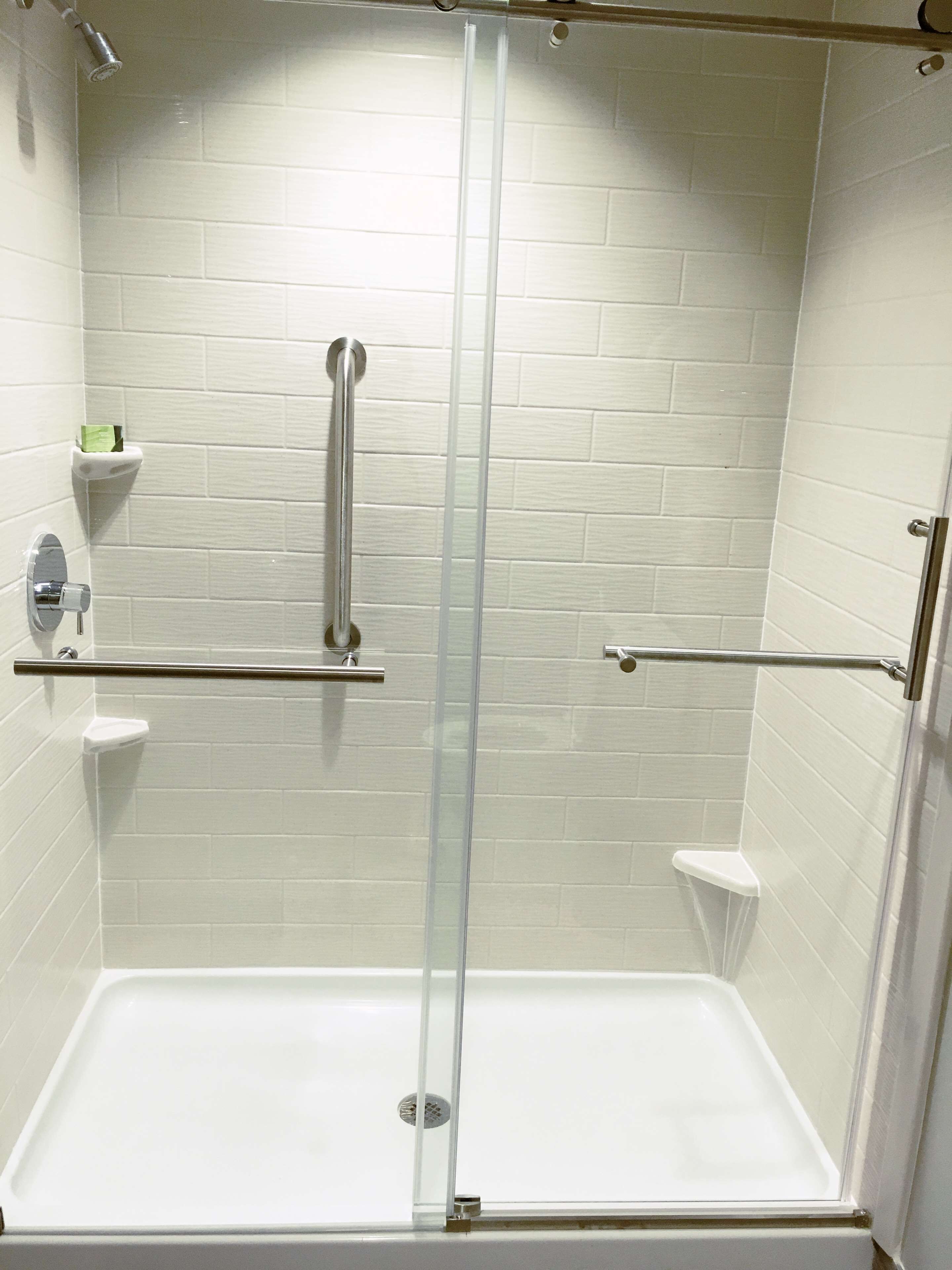 A shower with a glass door, white tiled walls, and a metal grab bar.