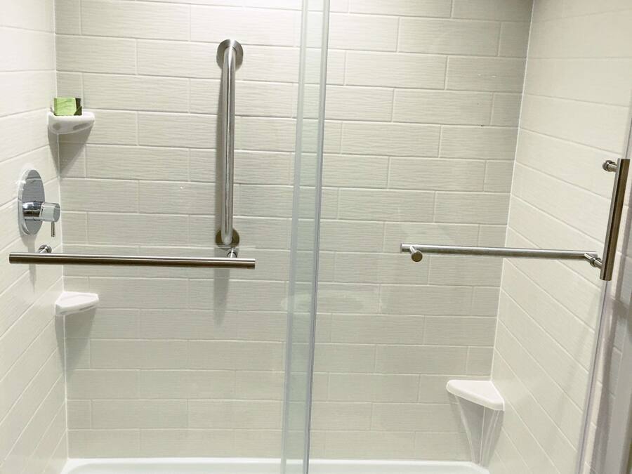 A shower with a glass door, white tiled walls, and a metal grab bar.