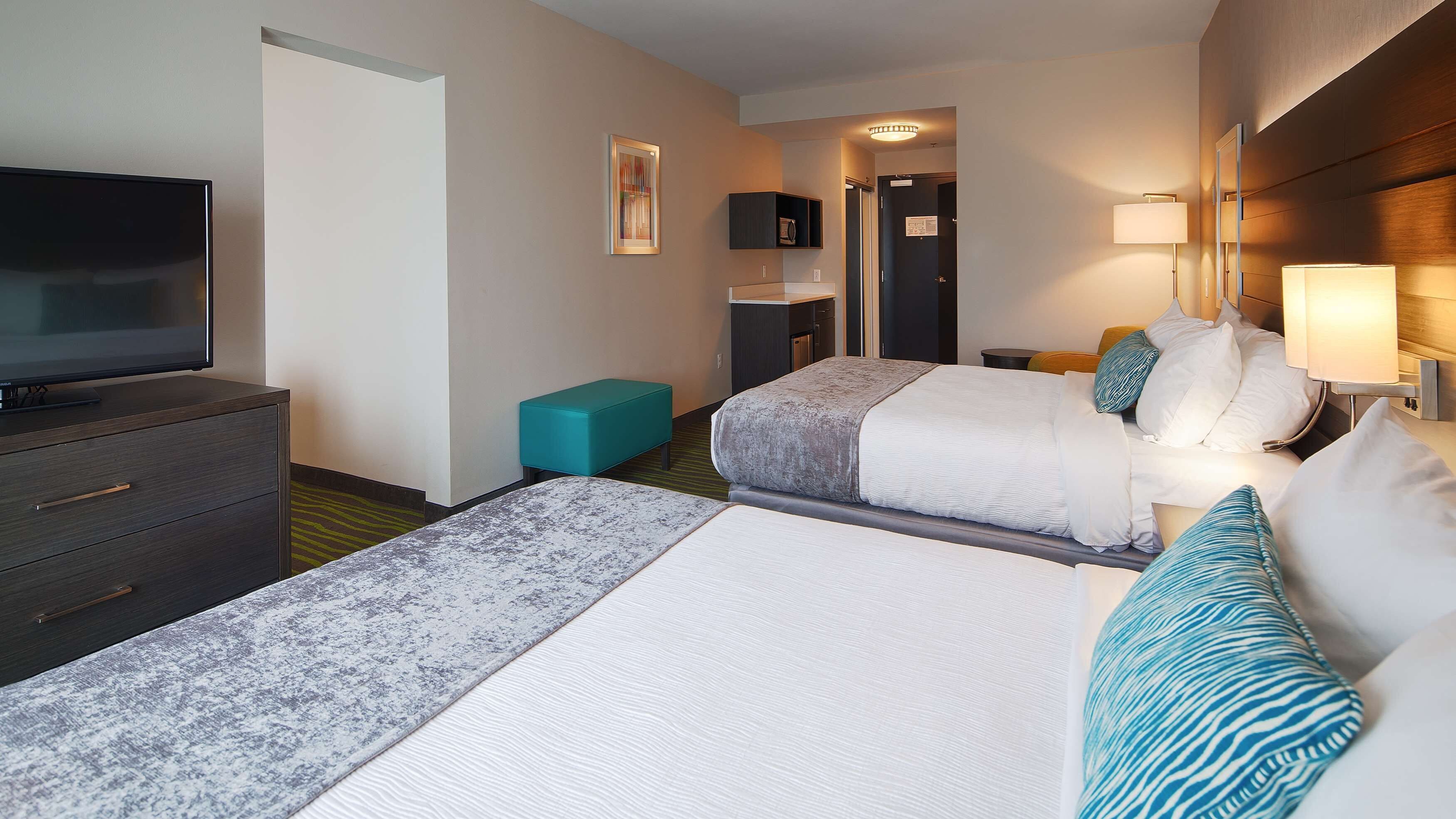 A hotel room with two beds, a television, a desk, and a bathroom.