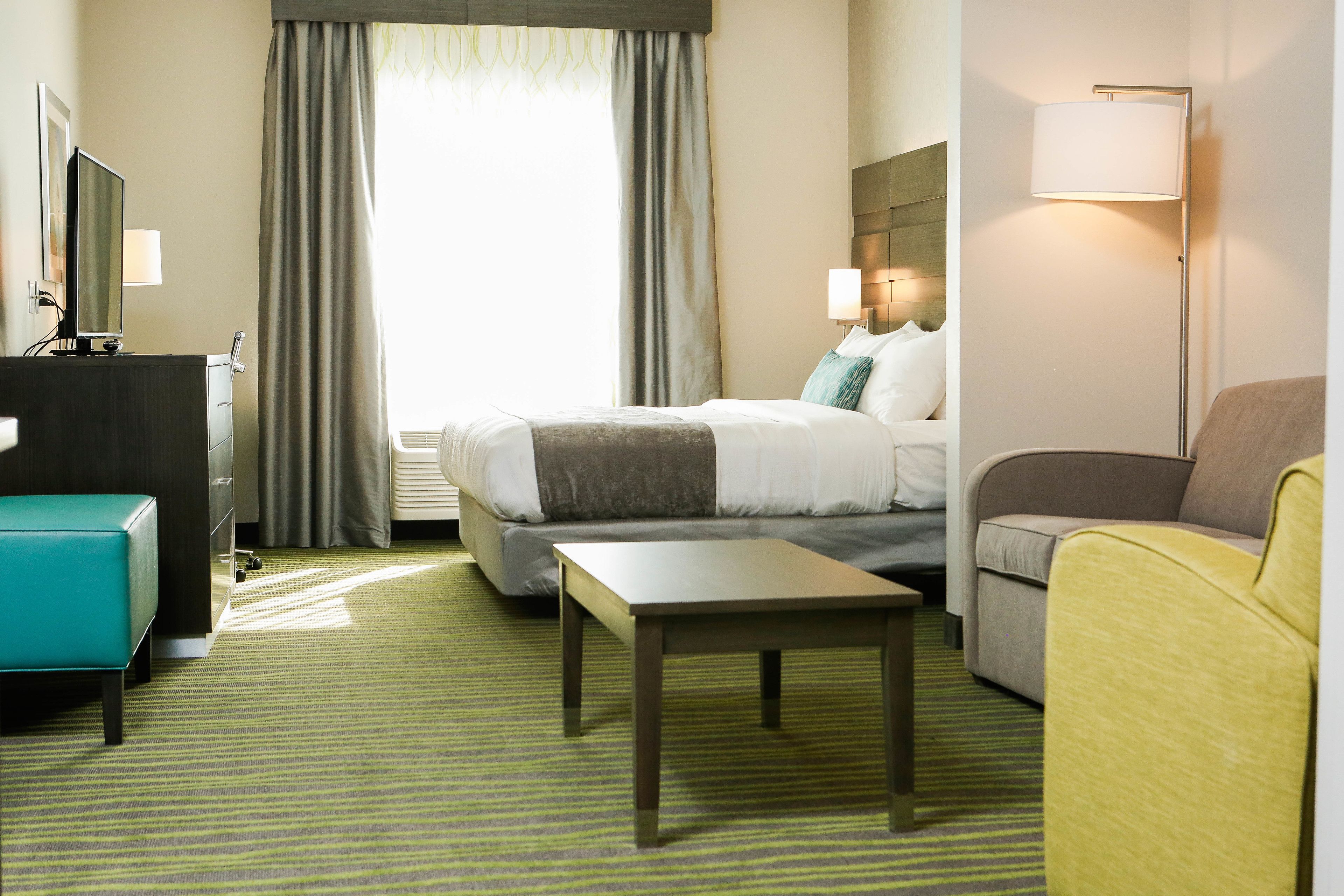 A hotel room with a bed, a desk, a chair, a sofa, and a lamp.