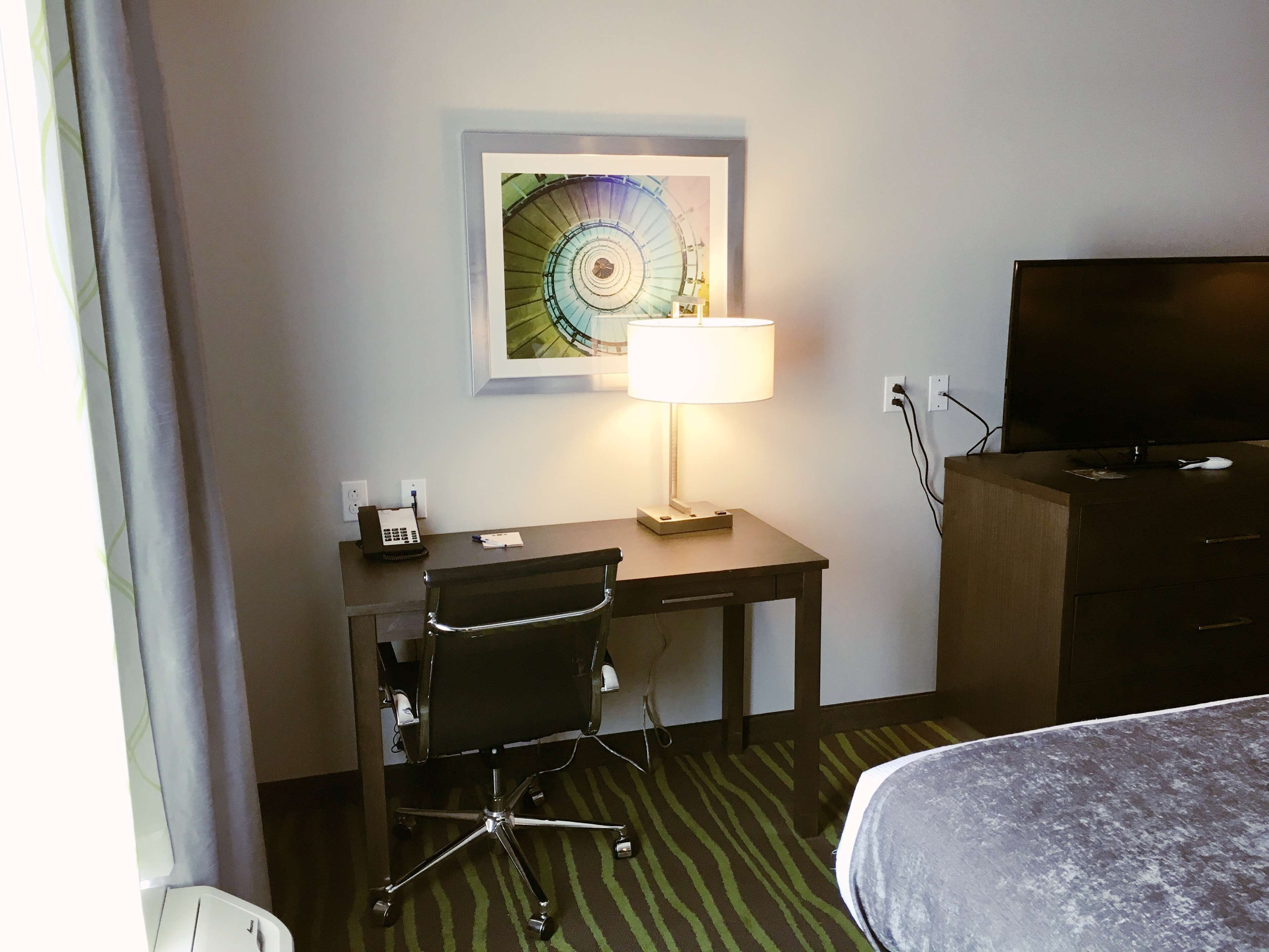 Una habitación de hotel con escritorio, silla, lámpara, televisor y cama.