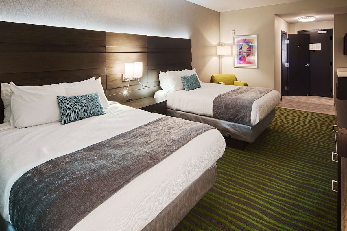 A hotel room with two beds, a green striped carpet, a TV, and a painting on the wall.
