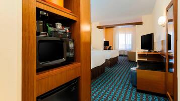 Habitación de hotel compacta con kitchenette, cama, televisión y alfombra estampada.