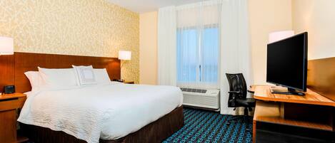A hotel room with a large bed, a desk with a computer, an air conditioning unit, and a television.