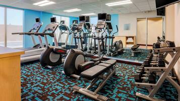 A gym with treadmills, elliptical machines, a bench press, and dumbbells.