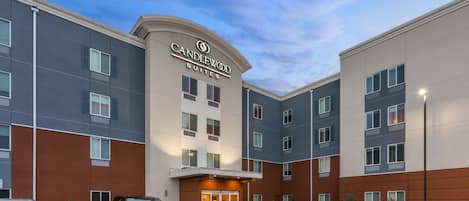A hotel with a modern facade, multiple floors, and a parking lot with vehicles.