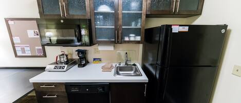 Una cocina compacta con lavavajillas, un refrigerador negro y un microondas.