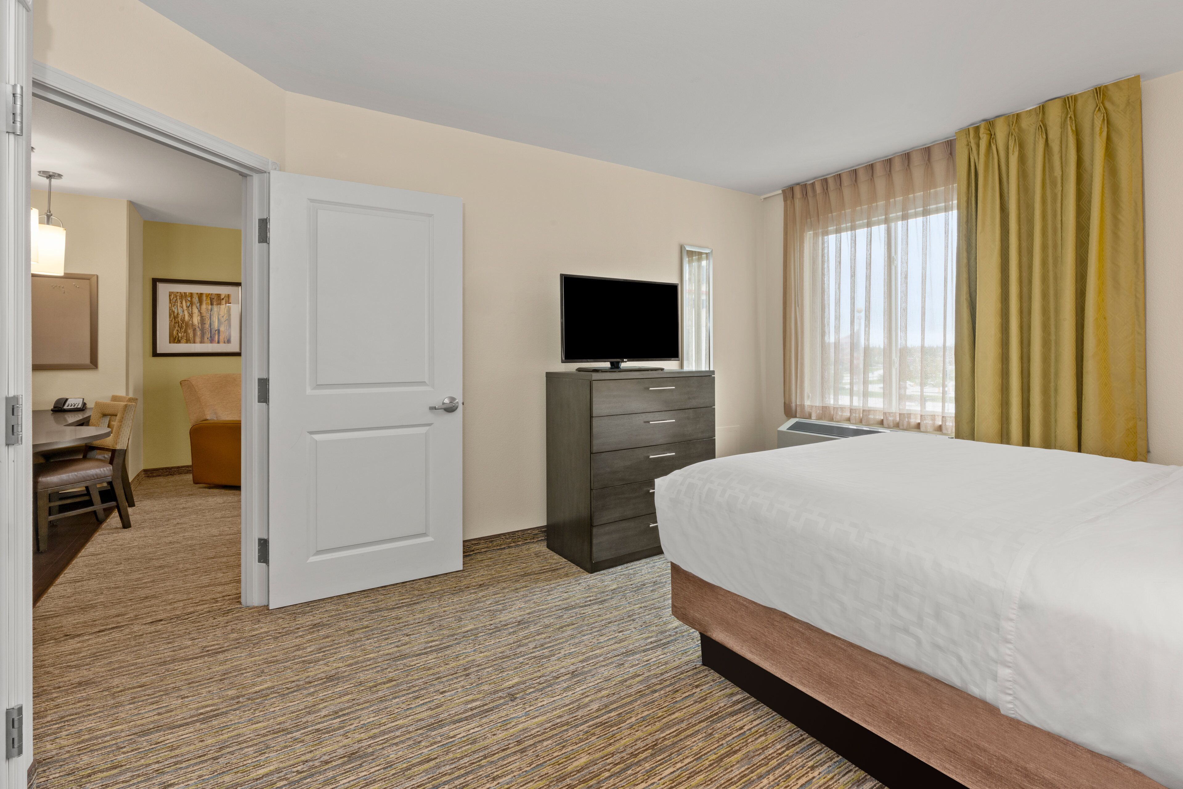 A hotel room with a bed, a dresser, a television, and a desk with a chair.