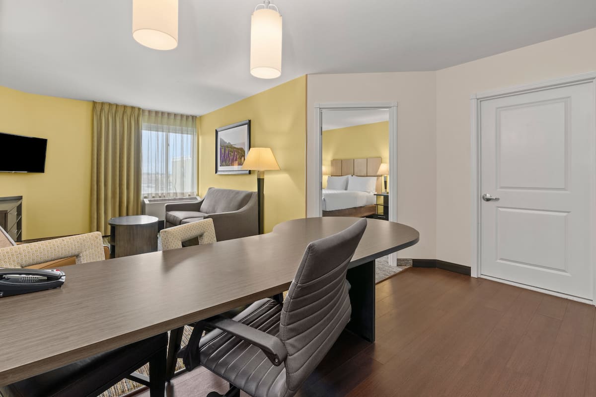 Une chambre d’hôtel avec un grand bureau, deux chaises, un lit, une télévision et une porte.