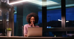 Une personne assise à un bureau, avec un ordinateur portable, une plante en pot et une fenêtre en arrière-plan.