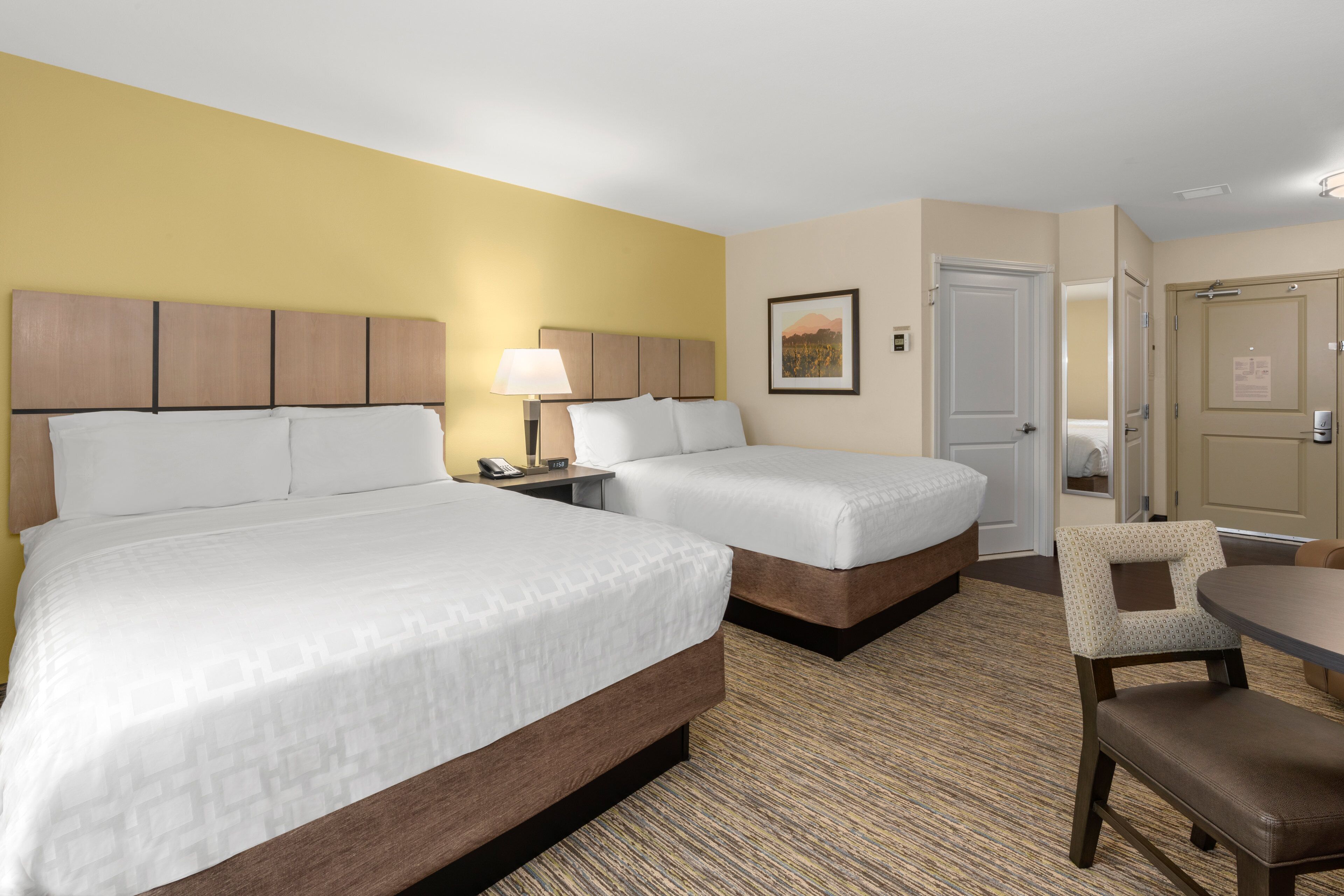 A hotel room with two beds, a desk, a chair, and a door.
