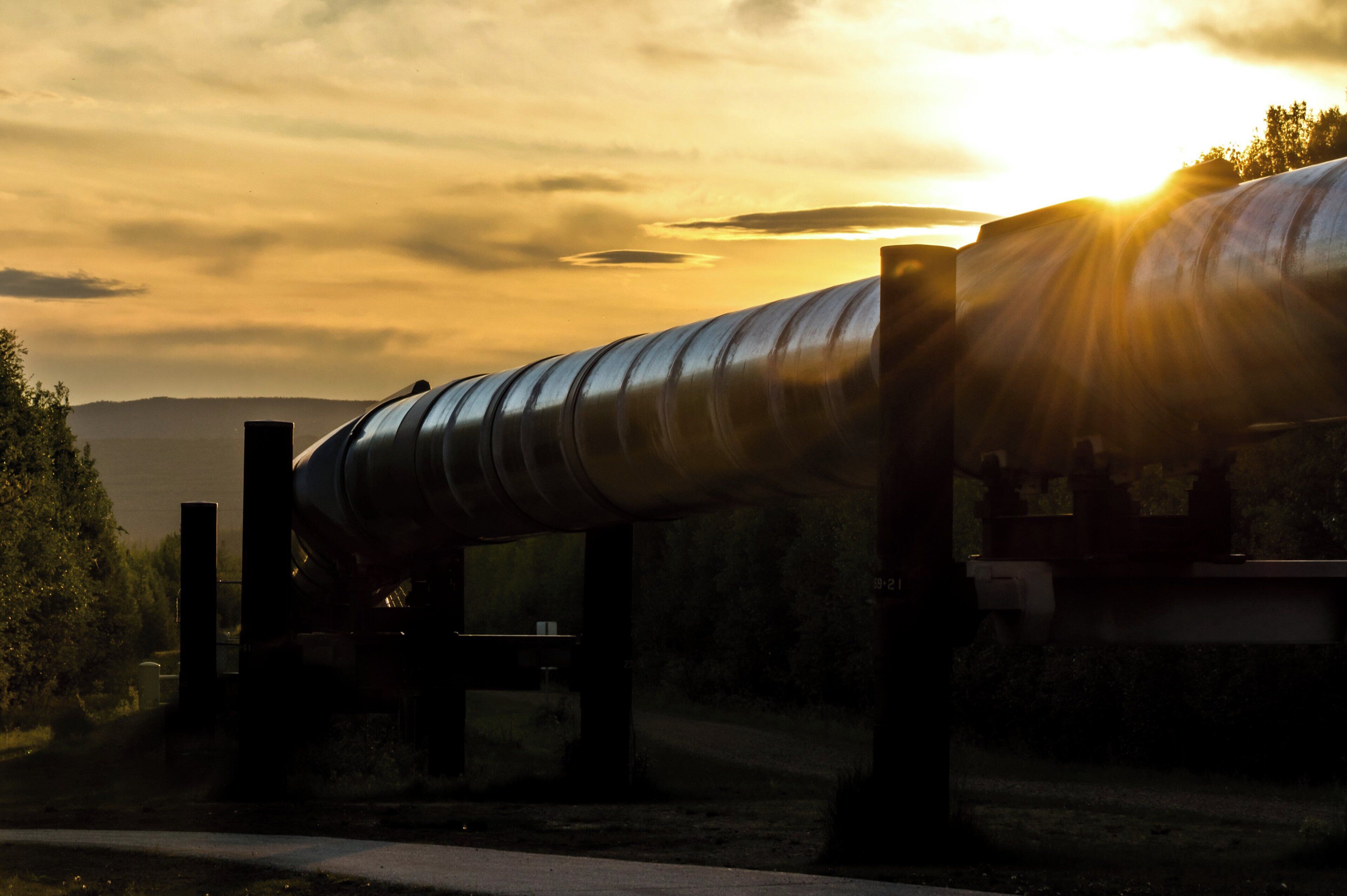 Una gran estructura de tubería industrial con diseño curvo, sostenida por vigas metálicas, con un cielo de atardecer y nubes de fondo.