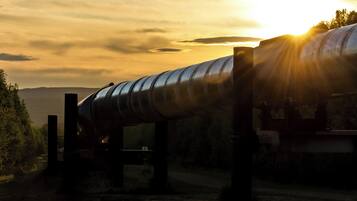 Una gran estructura de tubería industrial con diseño curvo, sostenida por vigas metálicas, con un cielo de atardecer y nubes de fondo.