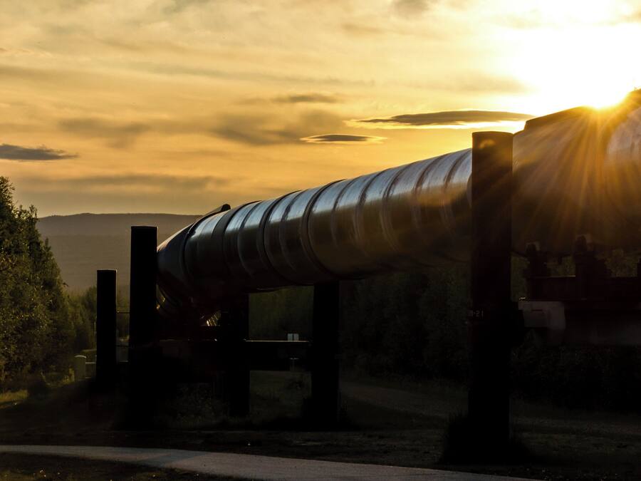 Una gran estructura de tubería industrial con diseño curvo, sostenida por vigas metálicas, con un cielo de atardecer y nubes de fondo.