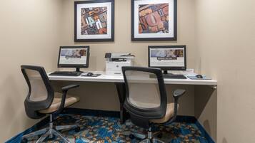 A workspace with three computers, two chairs, and framed artwork on the wall.