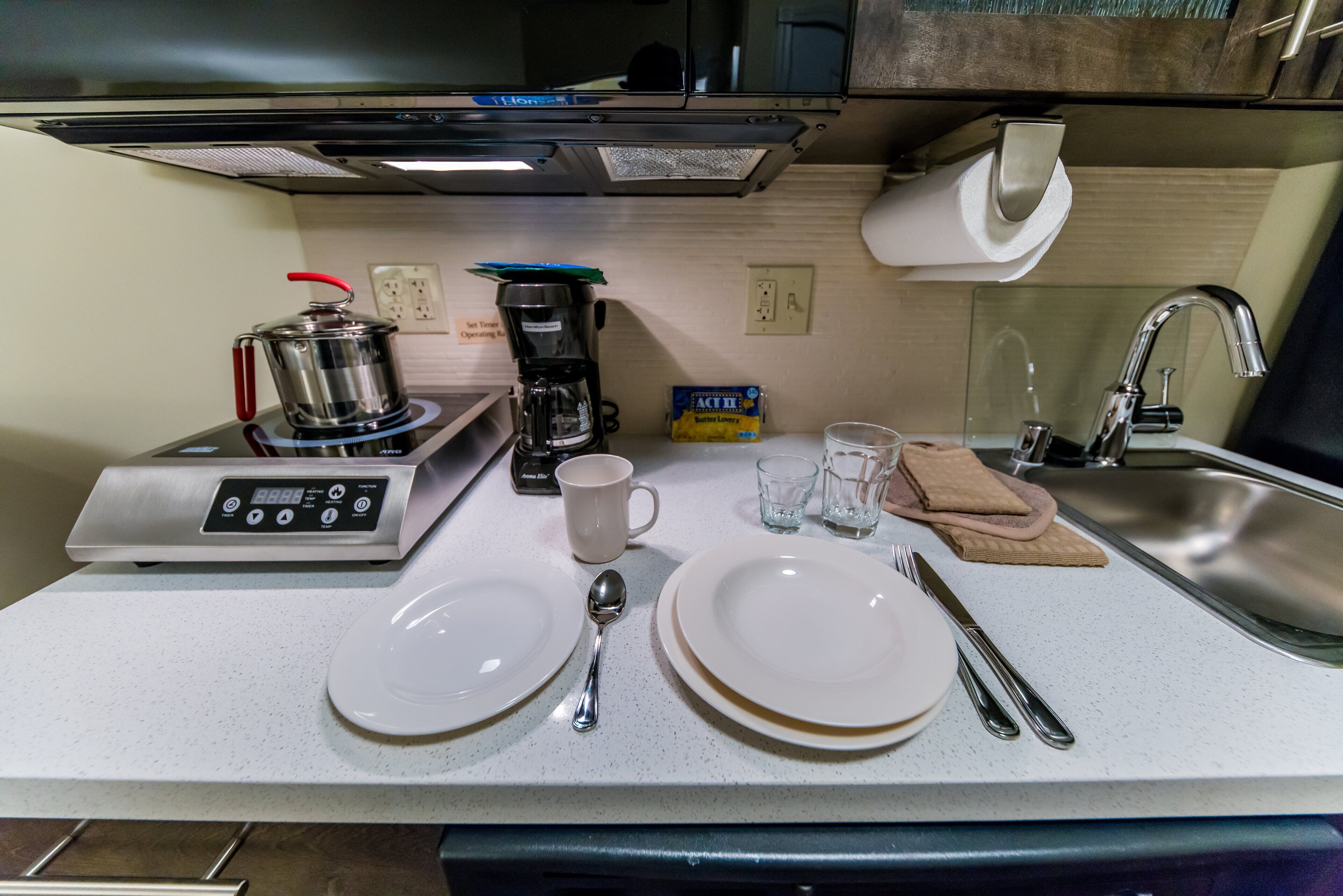 A compact kitchenette with a stove, coffee maker, and a sink.