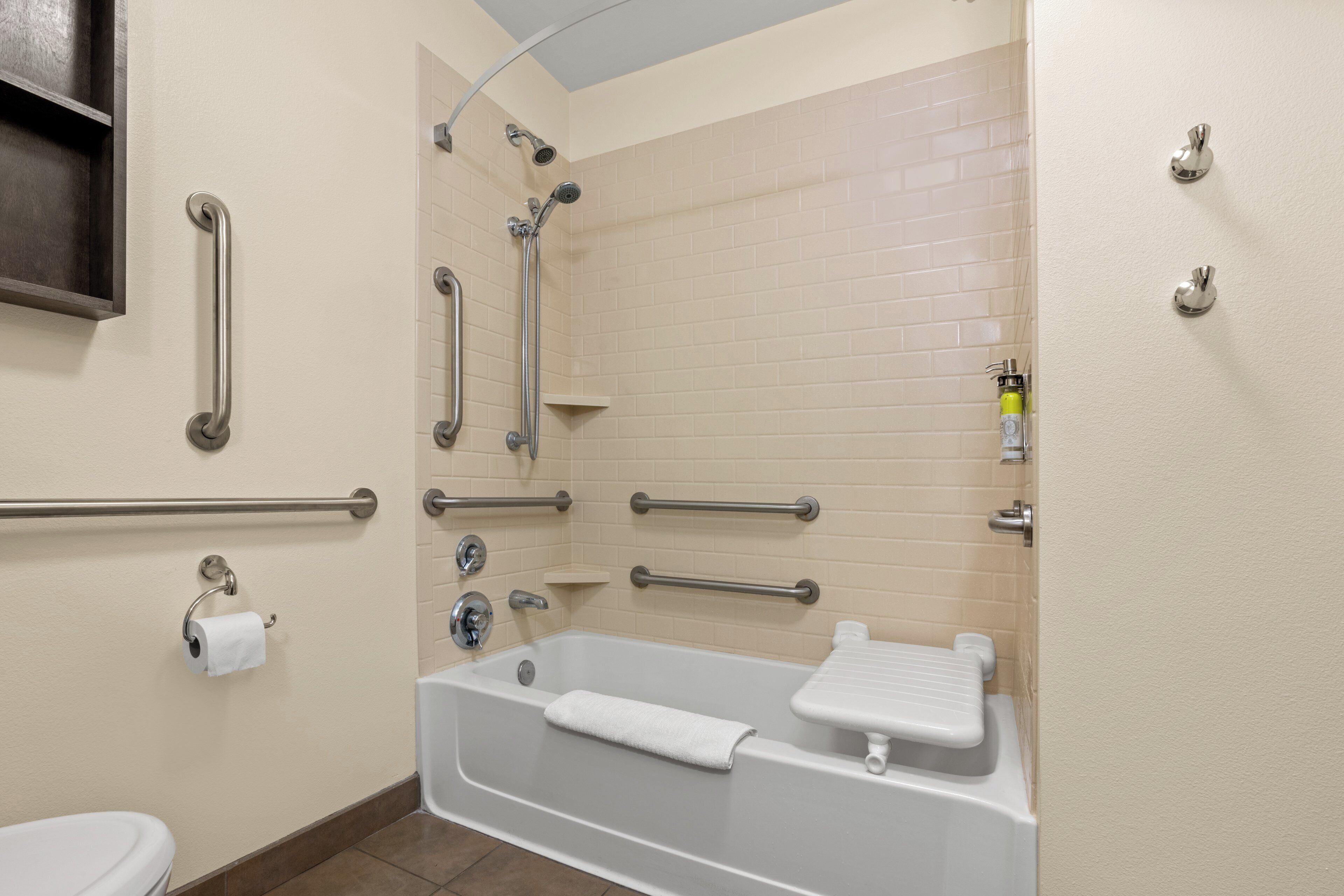 Ein Badezimmer mit Badewanne, Haltegriffen, Toilette und Dusche inklusive Duschbrause.