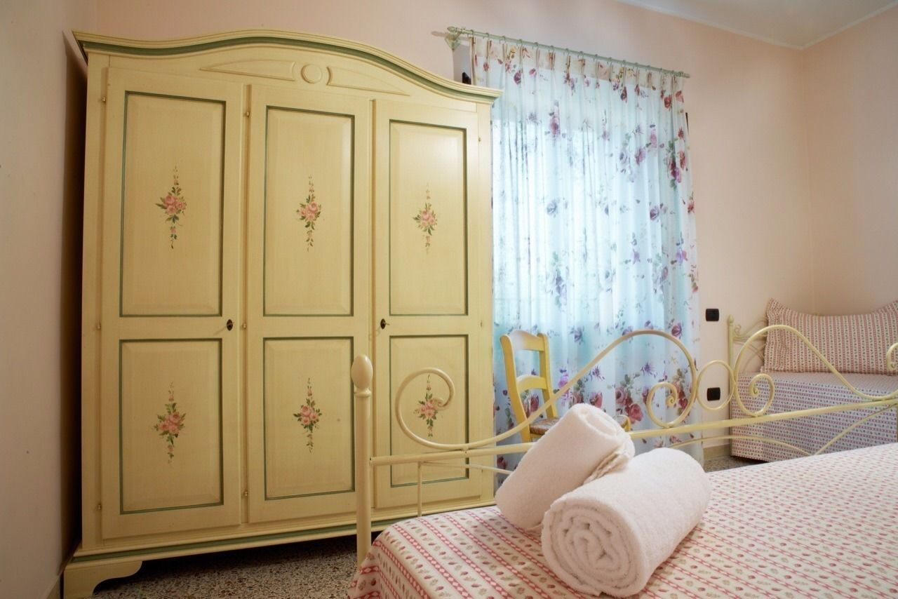 Une chambre à coucher avec un lit, un lit à ossature métallique, une armoire jaune ornée de motifs floraux et un rideau à fleurs.