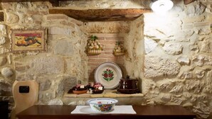 A rustic stone wall with a wooden shelf holding decorative items, a framed picture, and a table with a bowl. - Agriturismo Il Casolare Di Nonno Mario (Manoppello)