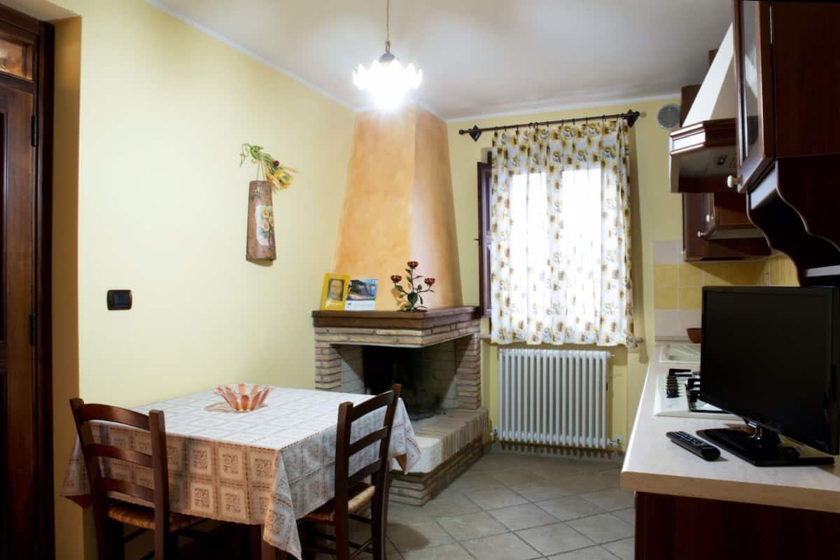 A compact kitchen with a built-in stove, a dining table with chairs, a television, and a window with curtains.