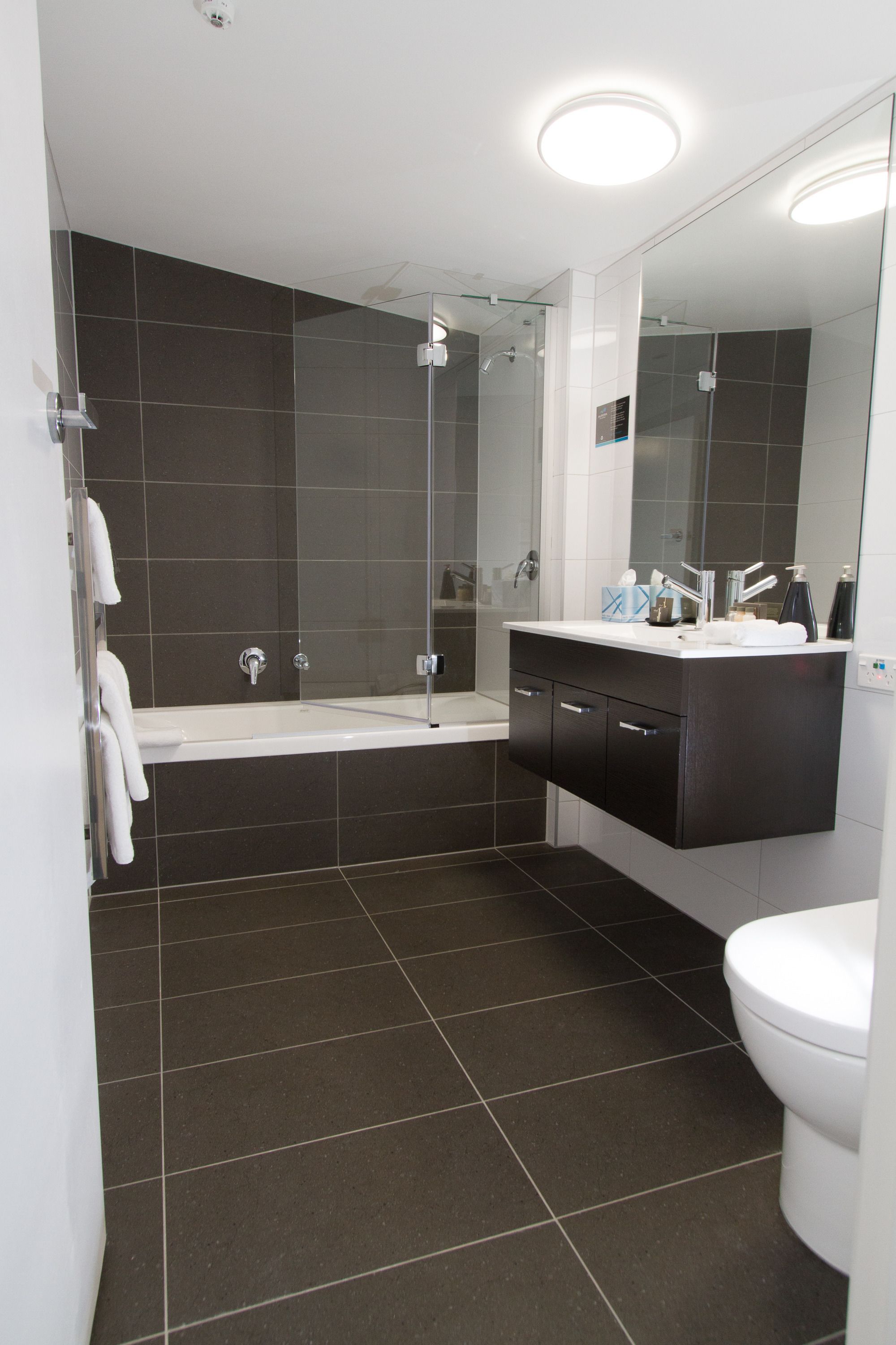 A modern bathroom with a glass-enclosed shower, a white bathtub, and a vanity with a mirror.