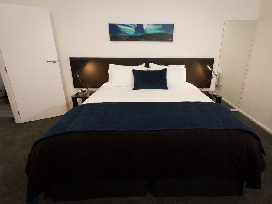 A hotel room with a large bed, a nightstand, a bedside lamp, a wall-mounted painting, and a door.