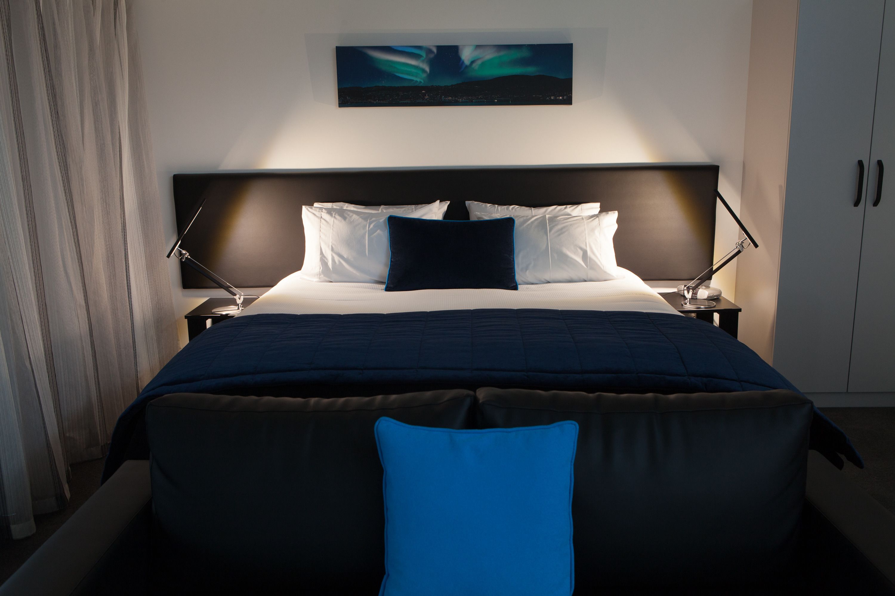 Ein modernes Hotelzimmer mit einem großen Bett, einem Nachttisch, einer Lampe und einem Gemälde an der Wand.
