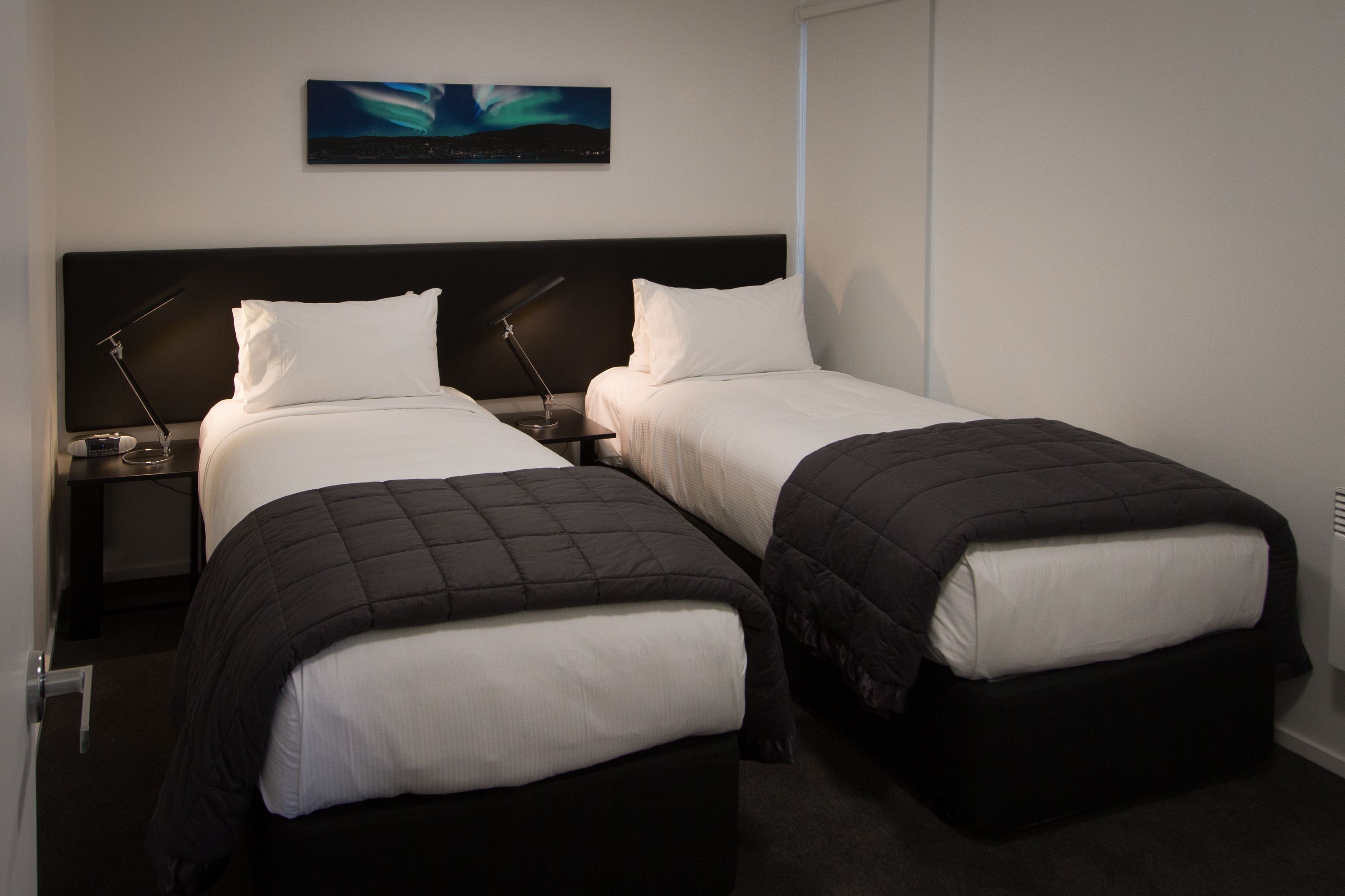Una habitación de hotel con dos camas individuales, una mesita de noche con lámpara y un cuadro en la pared.