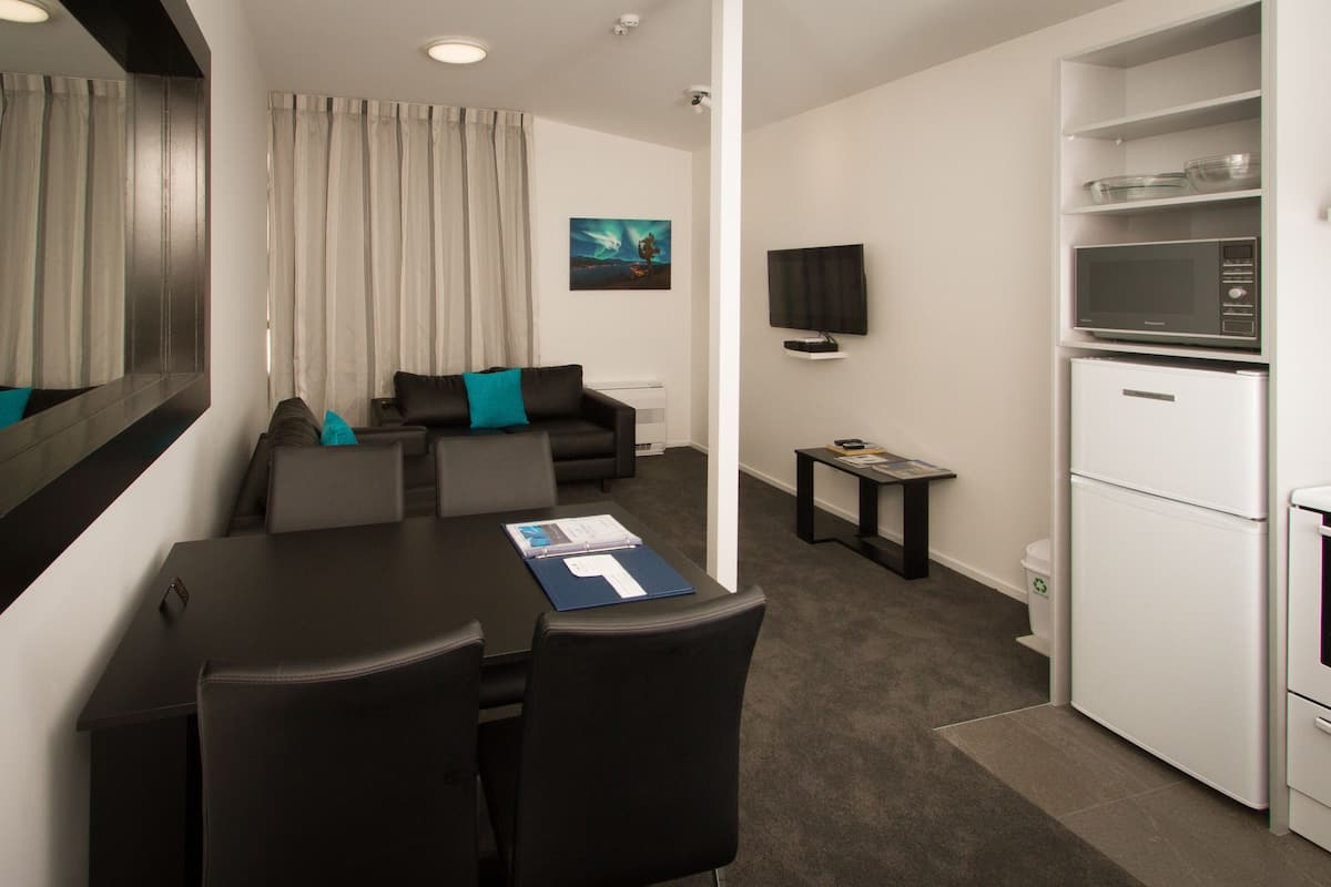 Una habitación de hotel moderna con zona de comedor, sofá, televisor de pantalla plana, microondas y refrigerador.