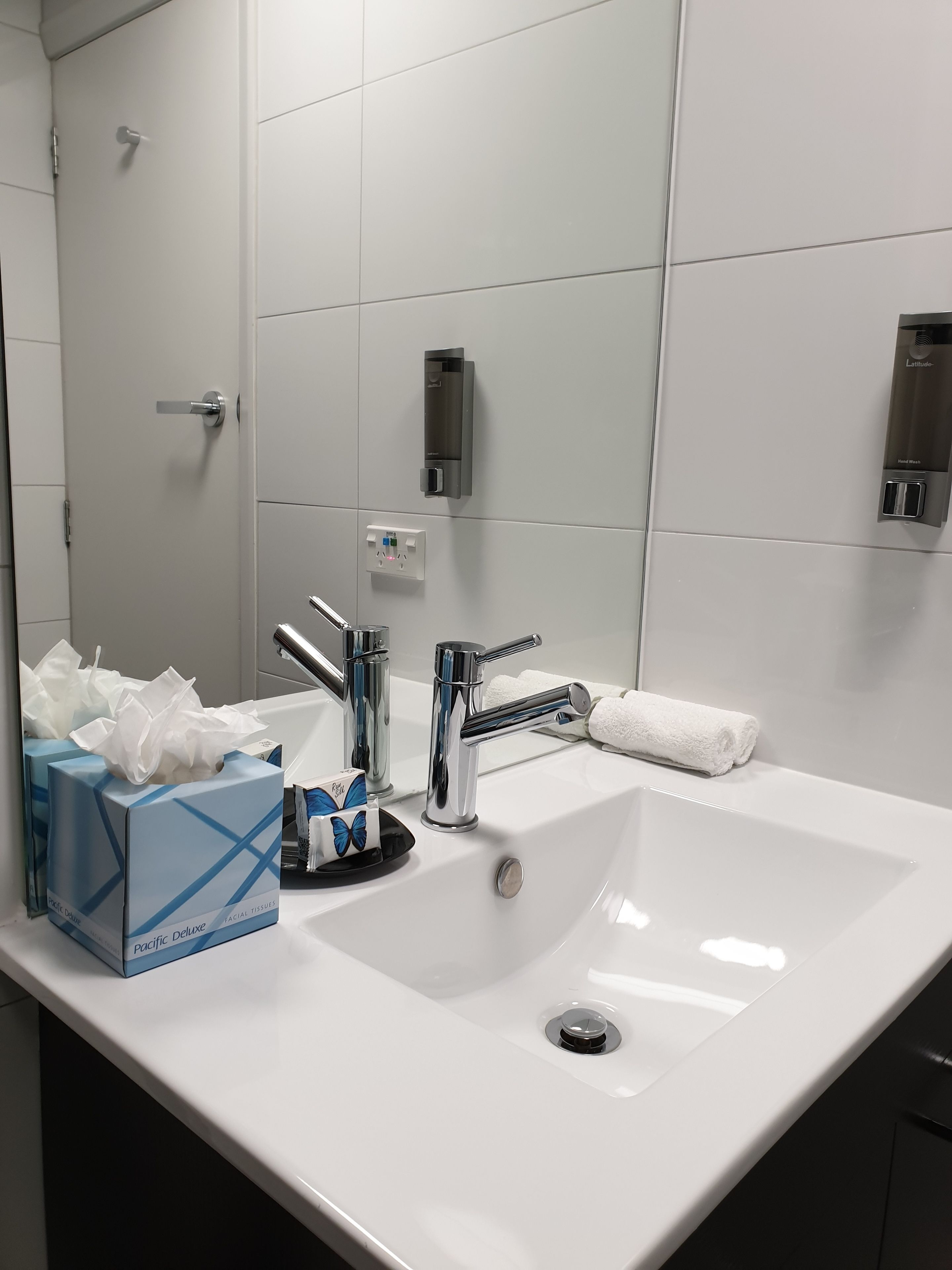 A modern bathroom with a white sink, chrome faucets, a mirror, and a hand dryer.