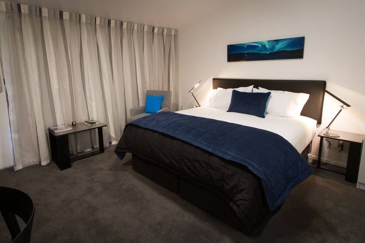 Habitación de hotel con una cama grande, un escritorio, una silla y una ventana con cortinas.