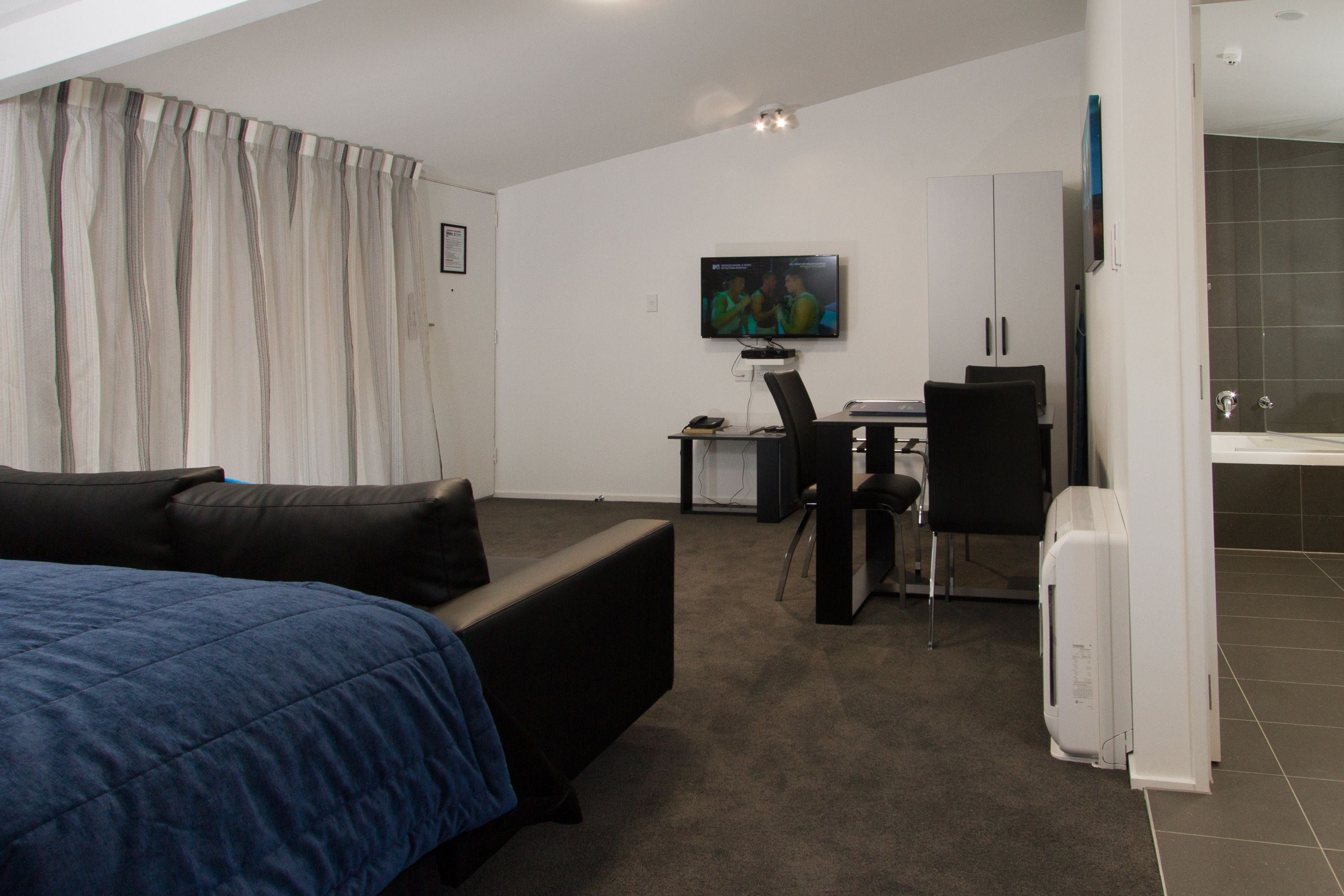 Una habitación de hotel moderna con una cama, un escritorio con una computadora, una silla y un televisor.