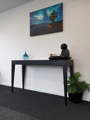 A dark wooden desk with a glass vase, a black object, and a potted plant against a white wall. - Aurora On George (Dunedin)