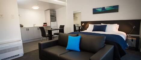 A modern hotel room with a bed, a sofa, a desk, and a kitchenette.