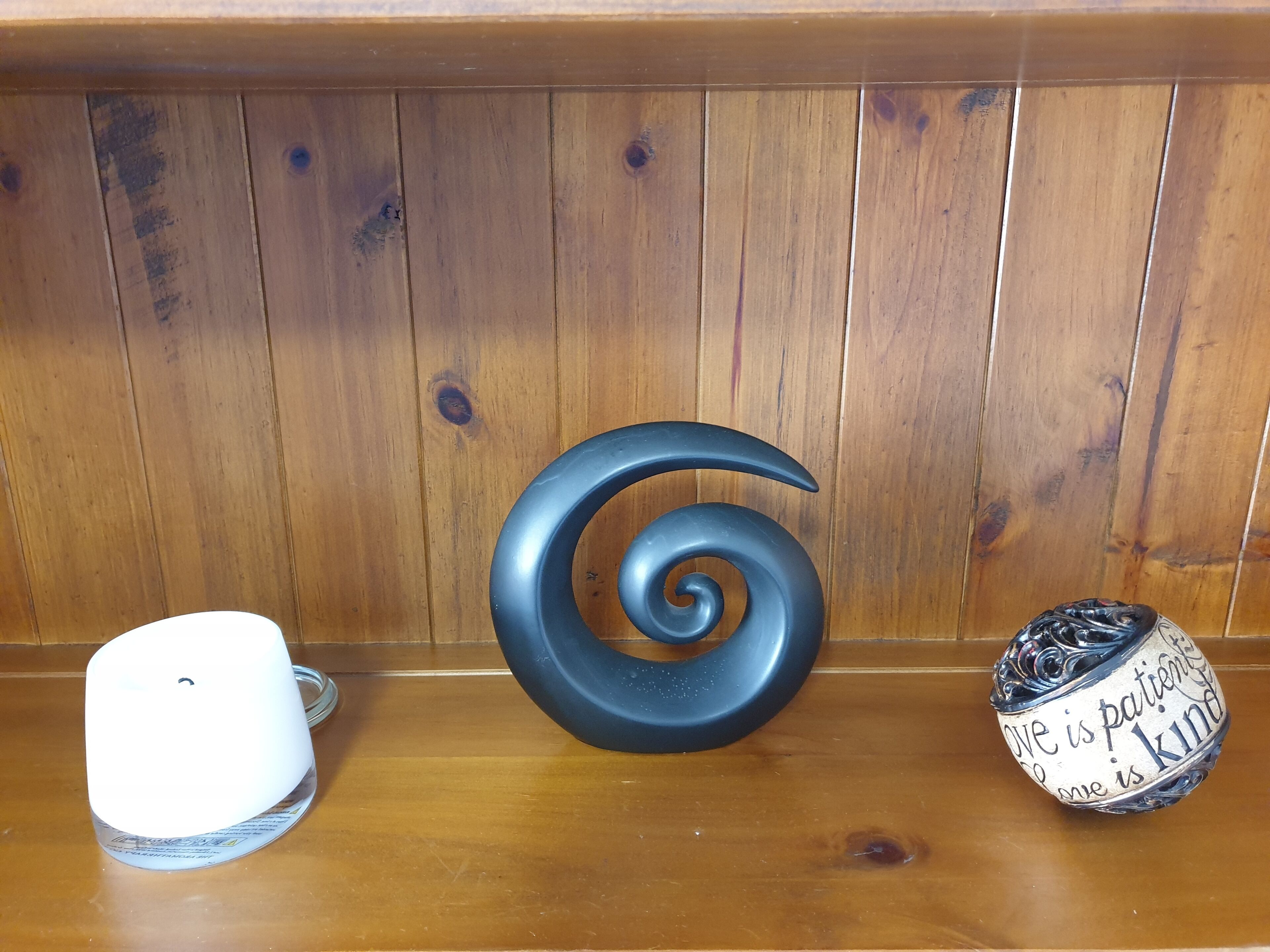Una estantería de madera con tres objetos decorativos: un objeto blanco, un objeto en espiral negra y una esfera decorativa con texto.