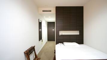 A hotel room with a bed, a wooden bench, a mirror, a door, and a wall-mounted shelf.