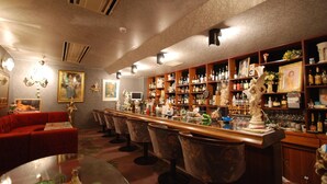 A bar area with a long counter, multiple bar stools, and shelves stocked with bottles.