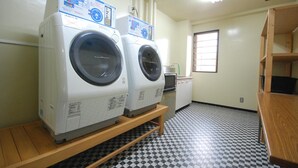 A laundry room with two front-loading washing machines on a wooden platform, a sink, and a window with bars.