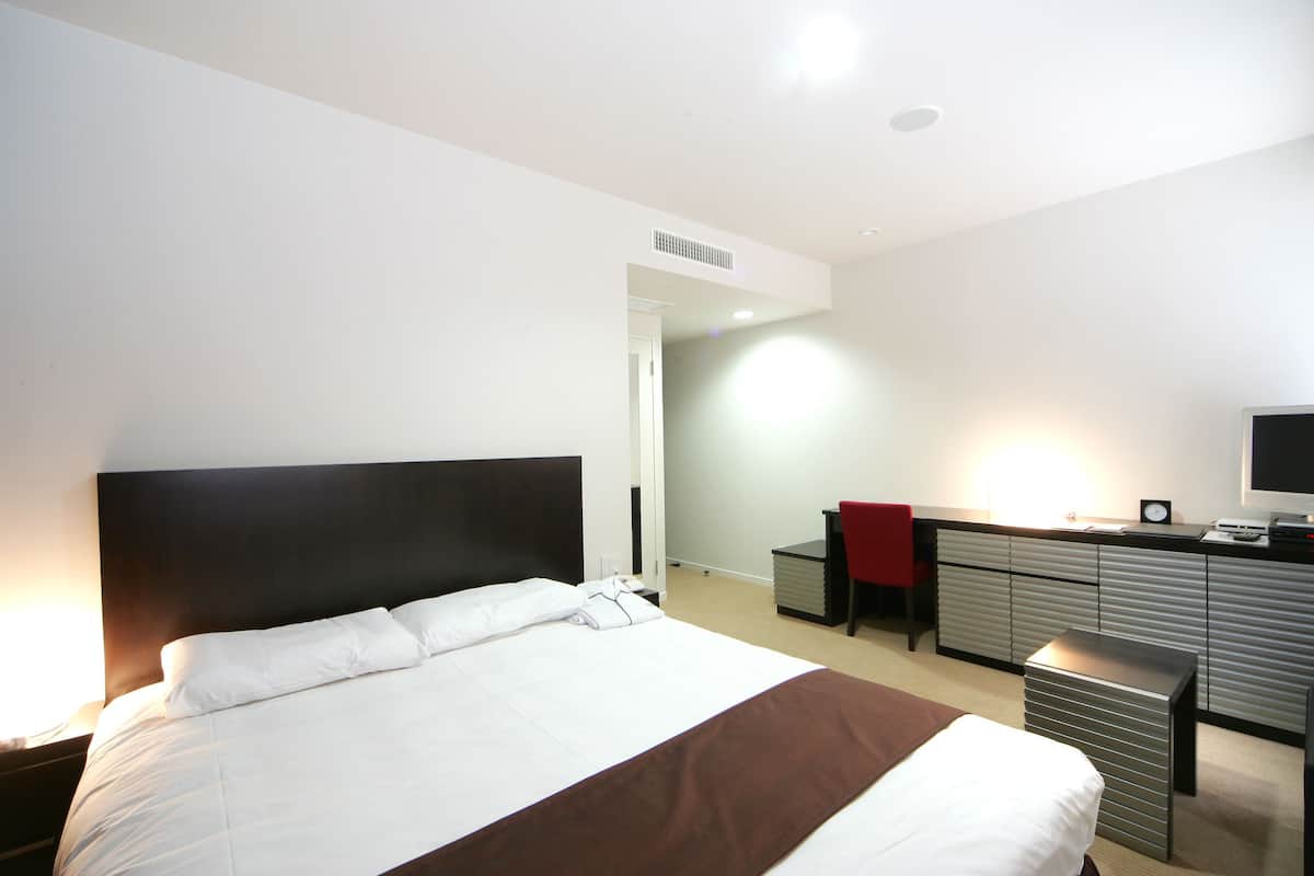 Une chambre d’hôtel avec un grand lit, un bureau avec une chaise, une télévision et une armoire.