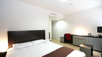 A hotel room with a large bed, a desk with a chair, a television, and a wardrobe.