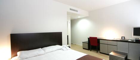A hotel room with a large bed, a desk with a chair, a television, and a wardrobe.